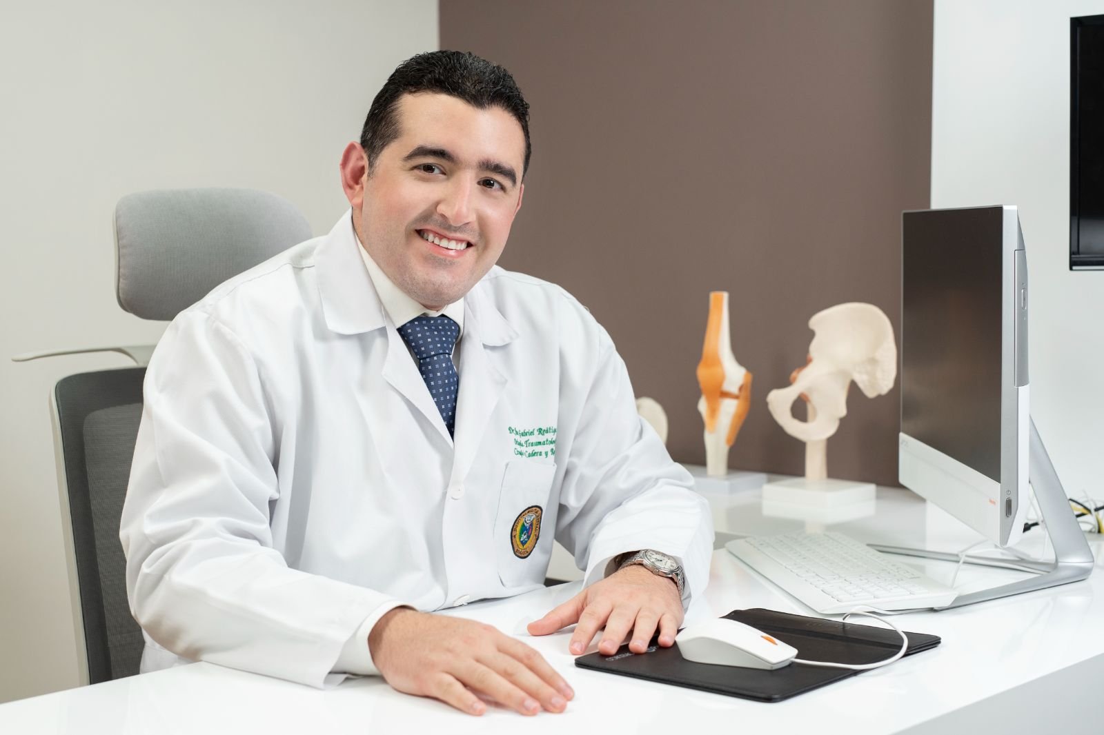 El Dr. Reátiga explica con modelos anatómicos de cadera y rodilla en su consultorio