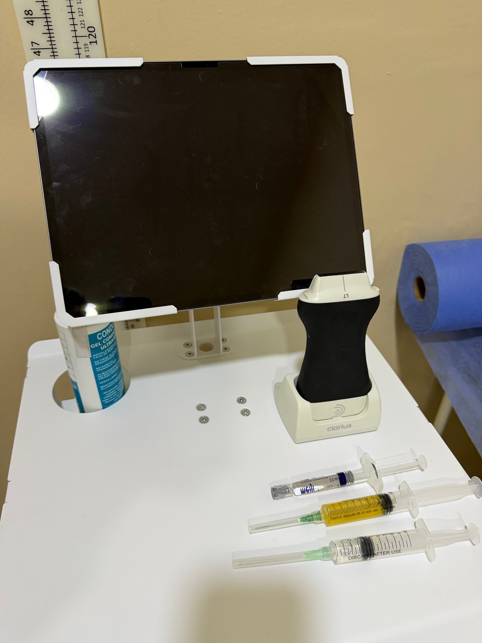 Ecografía de rodilla en el consultorio: el transductor sobre la piel y la imagen en vivo en la pantalla
