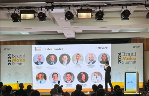 El Dr. Reátiga en el escenario del Brasil Mako Summit 2024 de Stryker, en São Paulo, con el panel de conferencistas en pantalla